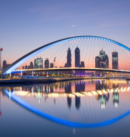 The Dubai skyline reflected on the water at sunset, with the iconic Midan Bridge in the foreground.