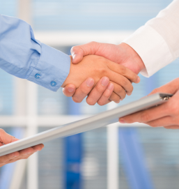 Two men shake hands and exchange a folder, symbolizing a business deal.